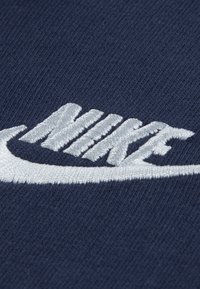 Mørkeblå tekstil med en fremtredende hvit brodert Nike-logo. Designet inkluderer en swoosh med diagonale, stiliserte bokstaver.
