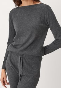 Maglione grigio lavorato a maglia con scollatura ampia e polsini a coste. Tessuto morbido, vestibilità rilassata, abbinato a pantaloni con coulisse coordinati.