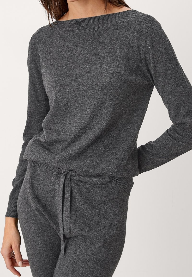 Maglione grigio lavorato a maglia con scollatura ampia e polsini a coste. Tessuto morbido, vestibilità rilassata, abbinato a pantaloni con coulisse coordinati.