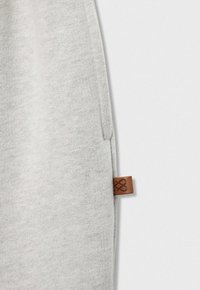 Jasnoszara dzianina z boczną kieszenią i małą brązową skórzaną metką wszytą w szew.