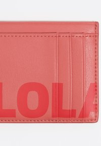 Tarjetero de cuero coral con cinco ranuras para tarjetas, texto en relieve "LOLA" y superficie texturizada. La costura contornea los bordes del diseño.