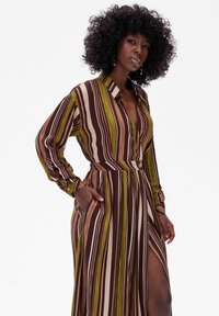 Pasiasta, długa sukienka z kołnierzykiem, z detalami w postaci guzików, długimi rękawami i bocznymi kieszeniami w odcieniach brązu, zieleni i kremu.