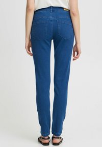 Sinine denimist valmistatud sirge jala disainiga püksid, kahe tagataskuga ja keskmise tõusuga vöökoht. Omab tekstuurset kangast ja õmmeldud vööd.