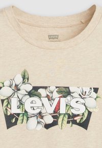 Beżowa bawełniana koszulka z ilustracją kwiatową przedstawiającą białe kwiaty magnolii, zielone liście oraz centralnym białym logo "Levi's".