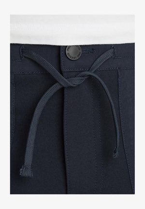 Mørkeblå badeshorts med snorelukning, flad talje og en lille sort logo-knap foran. Glat tekstur.