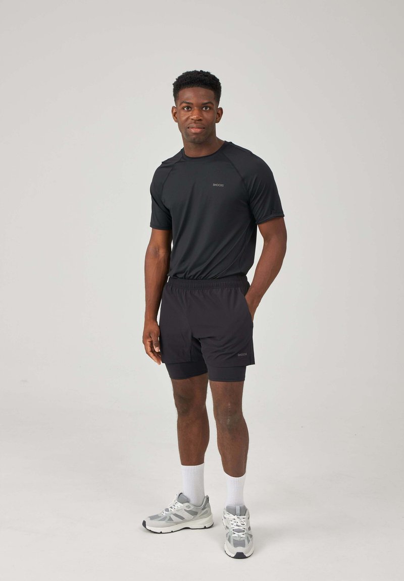 Black athletic t-shirt and shorts, with a relaxed fit. The material is smooth, lightweight, and moisture-wicking. Gray sneakers with white soles.