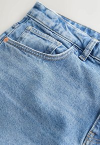 Jeans in denim blu chiaro con una finitura testurizzata, dotati di una vita, cuciture visibili e un piccolo dettaglio della tasca anteriore.