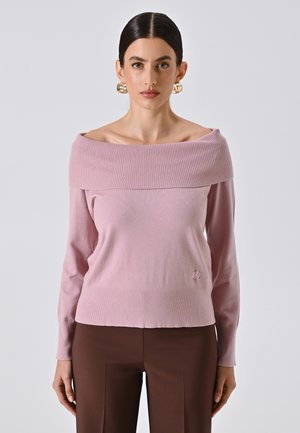 Hellrosa, schulterfreier Pullover mit geripptem Halsausschnitt und langen Ärmeln, mit einem dezenten Logodetail am Saum. Getragen mit braunen Hosen.