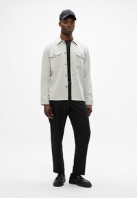 Ανοιχτό γκρι πουκάμισο με δύο τσέπες στο στήθος, μαύρη μπλούζα από κάτω και μαύρο παντελόνι, συμπληρωμένο με μαύρα παπούτσια και καπέλο.