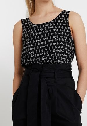 Top senza maniche nero con motivo a rombi bianchi, scollatura rotonda e vestibilità ampia. Abbinato a pantaloni neri a vita alta con una cintura annodata.