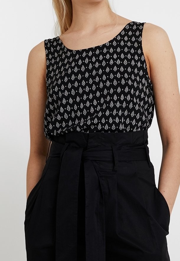 Top senza maniche nero con motivo a rombi bianchi, scollatura rotonda e vestibilità ampia. Abbinato a pantaloni neri a vita alta con una cintura annodata.