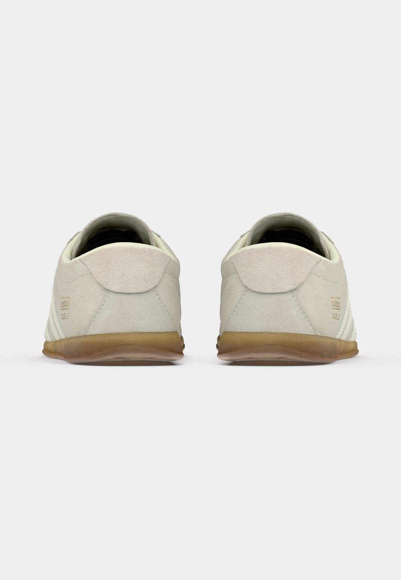 Light beige sneakers with a suede texture, featuring a rounded toe, rubber sole, and subtle tonal stitching along the side.