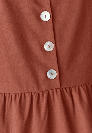 Tejido de color óxido con un acabado texturizado, que presenta cinco grandes botones redondos e iridiscentes y un volante fruncido en el dobladillo.