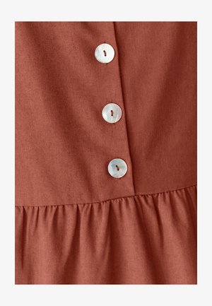 Rostetud kangas tekstuuriga pinnaga, millel on viis suurte ümmarguste iridessentsete nööbiga ja koondunud volang allääres.