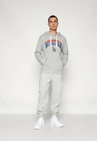 Sweatshirt cinzenta com texto "DODGERS" em azul e vermelho, calças cargo cinzentas e ténis brancos. Apresenta capuz e bolsos frontais.