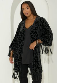 Svart sammet kimono med lövmönster, öppen front, vida ärmar och fransar i nederkant. Lättviktsmaterial med slät textur.