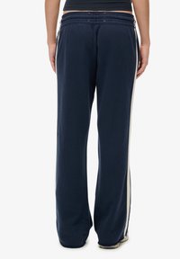 Mørkeblå sweatpants med afslappet pasform, elastisk talje og hvide sidestriber. Blødt stof med subtil tekstur, velegnet til afslappet brug.