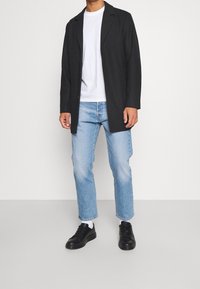 Blazer negro de manga larga sobre una camiseta blanca, combinado con jeans rectos de mezclilla azul claro y zapatillas negras. Tela suave y ajuste relajado.