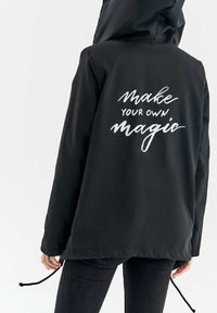 Čierna mikina s kapucňou a sťahovacím lemom. Na zadnej strane je biele písmeno: "Vytvor si svoj vlastný zázrak." Hladká tkanina, voľný dizajn.