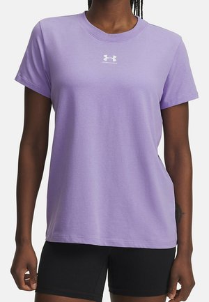 Personne portant un t-shirt à manches courtes Under Armour lavande et un short noir, debout, les bras détendus le long du corps.