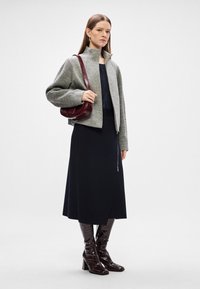 Γκρι πλεκτό μπουφάν με φερμουάρ και ριχτές μανσέτες, συνδυασμένο με μπλε μάξι φούστα που έχει πλαινό φερμουάρ, και γυαλιστερά μποτάκια σε μπορντό μέχρι το γόνατο.