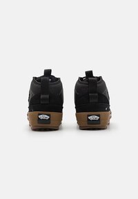 Sorte høye sneakers med en teksturert stoffoverdel, gummisåle og en gummisåle. Har Vans-merke på hælen og bakre flik.