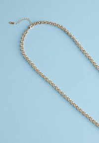 Gold chain necklace with round links and adjustable clasp laid on light blue background.