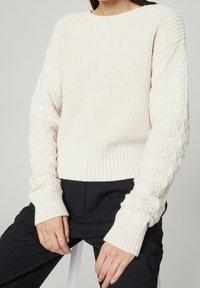 Gebreide crèmekleurige trui met geribbelde zoom en manchetten; textuurrijk mouwontwerp met diamantmotief; zacht materiaal; ontspannen pasvorm.