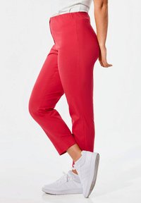 Rode stretchbroek met een hoge tailleband, taps toelopende broekspijpen en een gladde textuur, gecombineerd met witte sneakers. Geen zichtbare zakken of patronen.