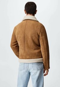 Brun ruskindsjakke med en cremefarvet shearlingkrave, der har et let afkortet design og synlige sømdetaljer på ryggen.