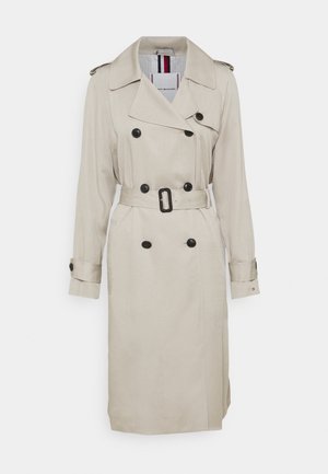 Beige dubbelgebreide trenchcoat met zwarte knopen, bijpassende riem met gesp, epauletten op de schouders en manchetten.