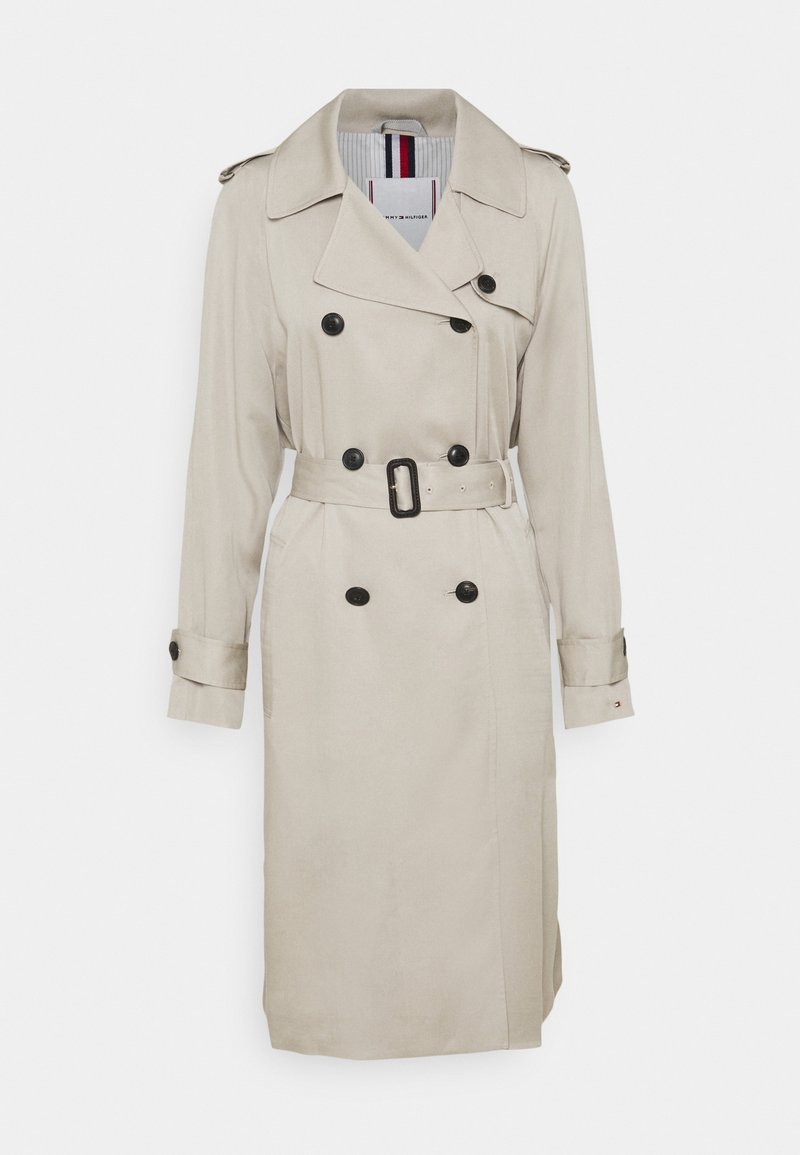 Trench-coat beige croisé avec des boutons noirs, ceinture assortie avec boucle, épaulettes aux épaules et brides aux poignets.