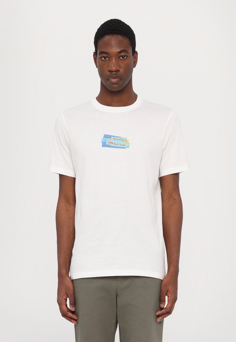 T-shirt blanc à manches courtes en coton doux. Présente un motif imprimé coloré sur la poitrine avec des éléments rectangulaires bleus et rouges.