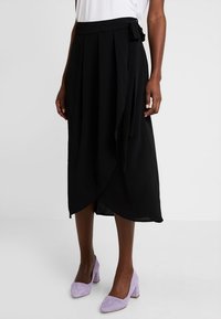 Svart omslagsskjorta i lätt tyg; har ett knytbart midjeband, plisseringar och en knälång nederkant med en något flödande design.