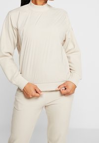 Beige Sweatshirt mit Rundhalsausschnitt, gerippten Bündchen und Saum, aus weichem Stoff, mit lockerer Passform und subtiler Textur.