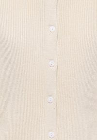 Krämfärgad ribbad cardigan i texturerad stickad tyg, med knäppning framtill med fem vita knappar.