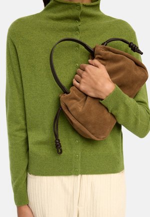 Osoba w zielonym swetrze na guziki trzyma przy piersi brązową zamszową torebkę z ciemnymi rączkami.
