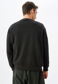 Sudadera negra con cuello y puños acanalados, que presenta una textura suave y un corte relajado, mostrada desde la parte trasera sin logotipos visibles.