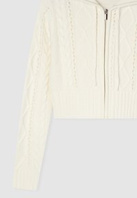Przycięty biały sweter z dzianiny z suwakiem, z wzorami w warkocze oraz ściągaczami na mankietach i u dołu. Miękka tekstura i ciepły materiał.