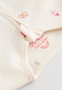 Body bébé crème clair avec des imprimés colorés et ludiques, en coton doux, doté de pressions et d'une finition à coutures plates. Étiquette rouge visible.