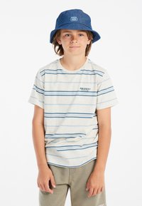 Gestreept t-shirt met korte mouwen in lichtcrème met blauwe horizontale strepen, gecombineerd met olijfgroene broek. Een blauwe bucket hat met logo-accenten.