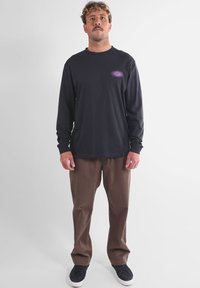 Chemise noire à manches longues avec un motif violet, pantalon marron et chaussures foncées. Design simple, matériau en coton, coupe décontractée et droite.