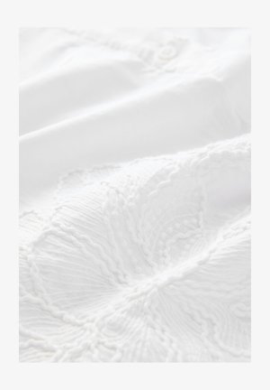 Tissu en coton blanc avec une broderie texturée complexe présentant un motif tourbillonnant et des détails subtils en relief. Comprend une fermeture à bouton.