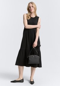 Schwarzes ärmelloses Kleid mit einem gestuften Rock, kombiniert mit schwarzen Ballerinas und einer kleinen Handtasche. Glattes Material, einfacher runder Ausschnitt und ausgestellte Silhouette.