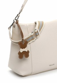 Cremefarvet læderhåndtaske med tekstureret overflade, med en stribet stofrem i beige, grå og hvid, samt en brun bamse-vedhæng.