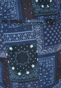 Kék árnyalatokban pompázó foltos rövidnadrág, bandana mintával, rugalmas derekkal. Elöl zsebet tartalmaz.