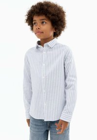 Cămașă cu dungi în albastru deschis �și alb, având guler deschis și mâneci lungi, purtată cu blugi din denim albastru.