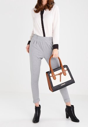 Blouse blanche avec accents noirs, pantalons gris fuselés, bottines noires et sac à main noir et crème avec poignées brunes et détail boucle.