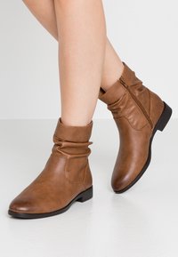 Bottines en cuir marron avec un design décontracté, fermeture éclair sur le côté, bout arrondi et un petit talon carré. Surface texturée avec une subtile brillance.
