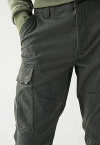 Dunkelgraue Cargo-Hosen aus weichem Stoff mit mehreren Taschen, einschließlich einer Seitentasche, und detaillierten Nähten. Slim-Fit-Design.